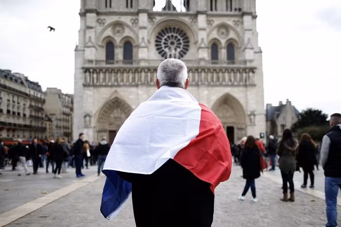 Một người đàn ông khoác trên mình quốc kỳ nước Pháp, lặng người khi đứng trước Nhà thờ Notre Dame ngày 16/11.