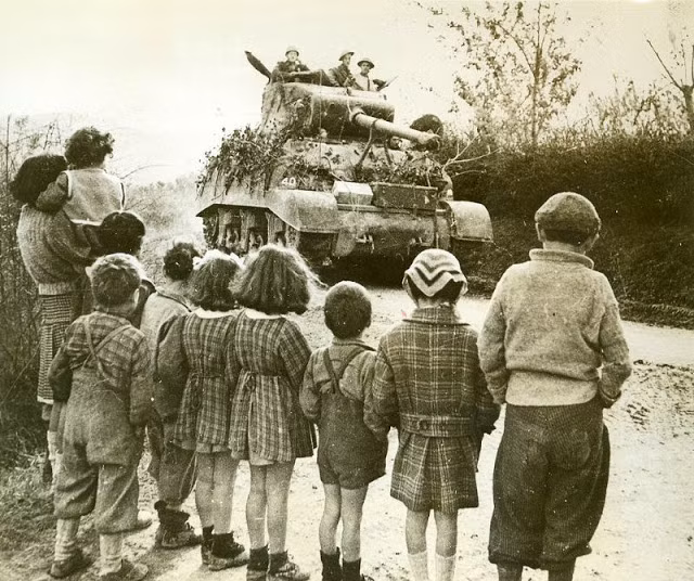 Trẻ em đứng xem cỗ xe tăng của quân đồng minh đi ngang qua nơi sinh sống.