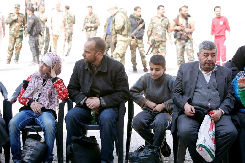 Những người dân đến từ thị trấn Douma ngồi chờ tại khu trại Wafideen ở Damascus hôm 13/3. Ảnh: Reuters.