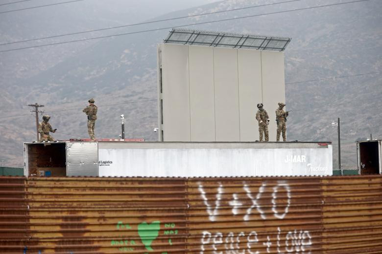 Cảnh sát Mỹ đứng trên nóc xe tải nằm mẫu tường biên giới mới và hàng rào biên giới hiện tại ở Tijuana, Mexico.