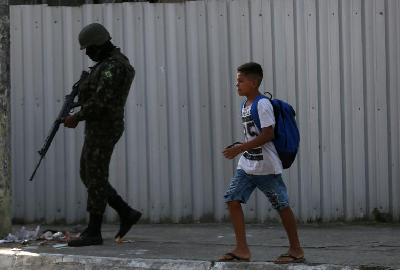 Bé trai đi qua binh sĩ Brazil tại khu ổ chuột Jardim Catarina.