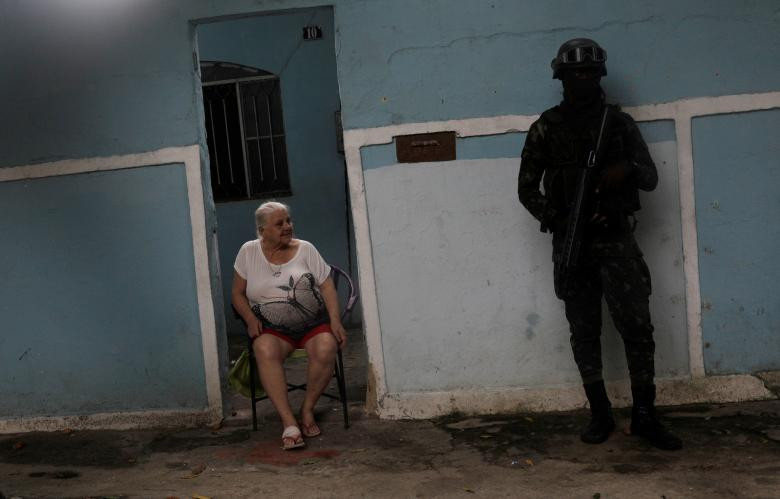 Một binh sĩ đứng trước nhà dân ở khu ổ chuột Vila Alianca, Rio.