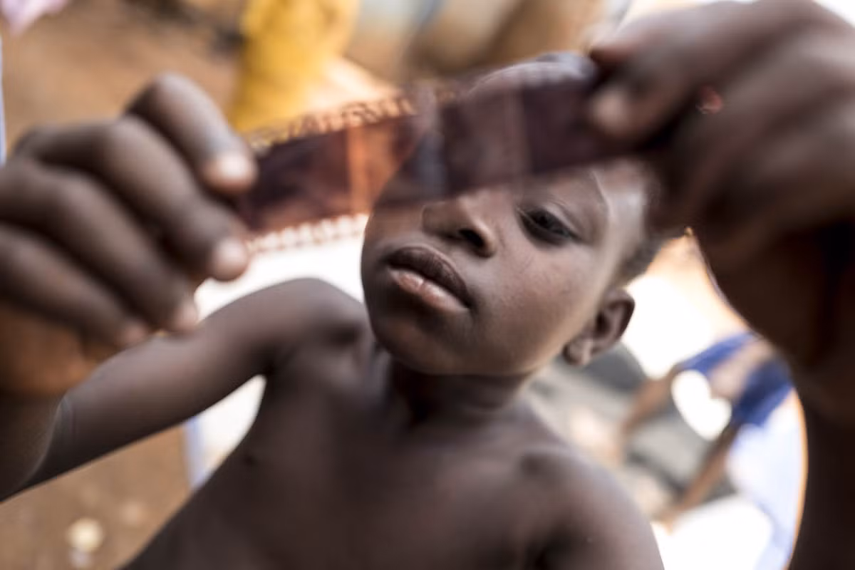 Isaac Newton, cậu con trai 9 tuổi của Nabwana, đang xem một cuộn phim âm bản của cha mình.