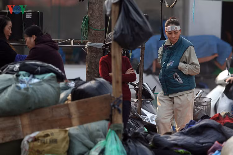 Một chị công nhân công ty vệ sinh môi trường tranh thủ nghỉ giải lao vào 1 “cửa hàng” bên vệ đường thử chiếc áo gi-lê cho mùa đông sắp tới gần.