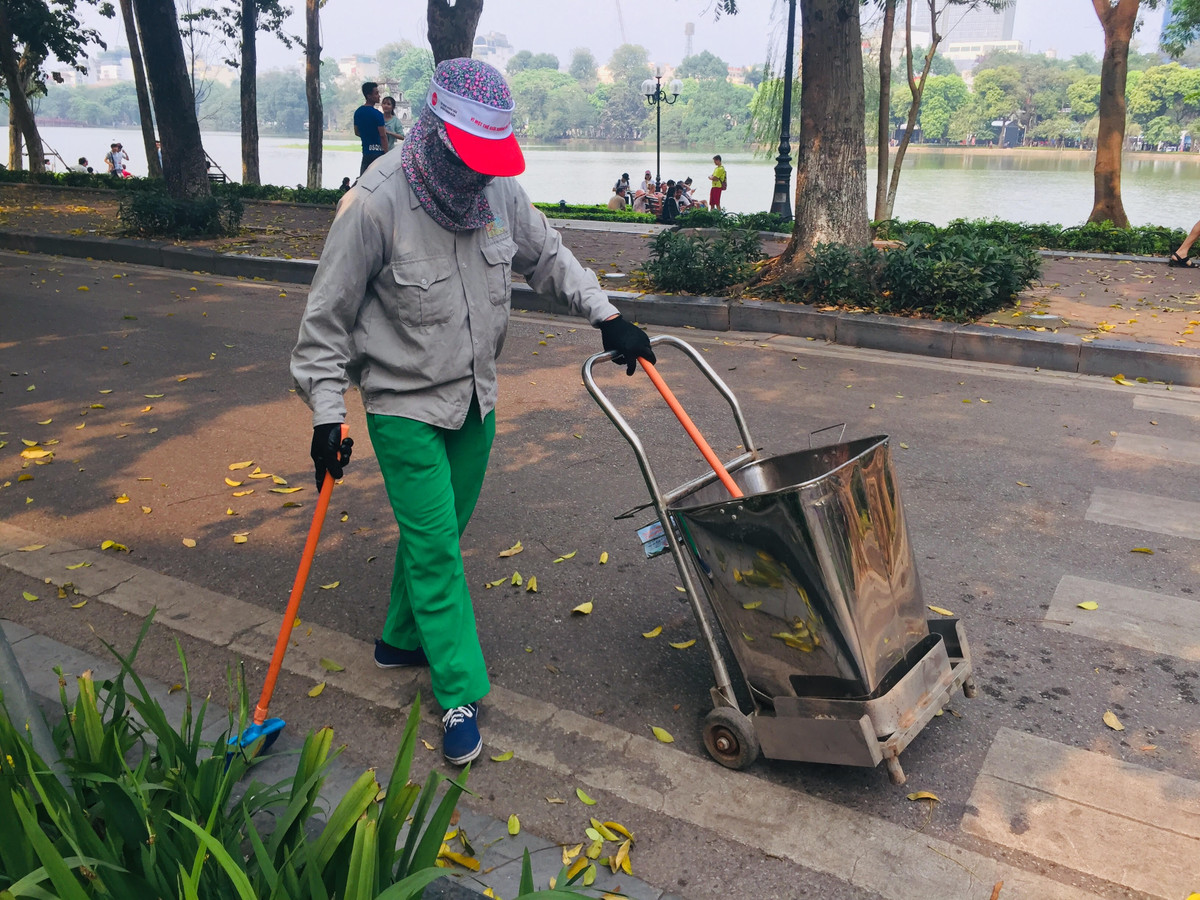 16h khi cái cũng dịu nhẹ phần nào nhưng khăn khố, áo dài bảo hộ, gang tay cũng được cô lao công ở phố Hàng Trống - Hà Nội che kín mít người. Cô bảo: “Mình ở đội U1 cơ, nay được điều sang đây hỗ trợ vì tháng này lá rụng nhiều mới nhiều sự kiện nữa”. 