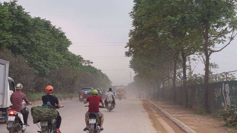 Trên tuyến đường thường xuyên xuất hiện xe tải hạng nặng lưu thông qua không che chắn theo quy định gây bụi bẩn. Trong ảnh người đi đường phải di chuyển chậm lại, tay bịt mũi để ngăn bụi