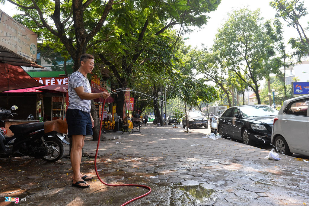 Anh Sơn, chủ một cửa hàng quần áo trên đường Hoàng Quốc Việt phun nước làm mát vỉa hè. Anh cho biết cửa hàng nhỏ, chật chội, việc phun nước ra vỉa hè giúp bên trong nhà đỡ nóng hơn.