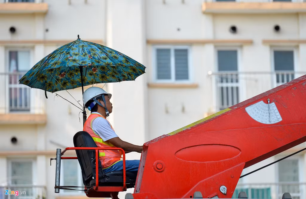 Công nhân lái cần cẩu trên đường Trường Chinh buộc một cái ô để tạo bóng mát. Do khu vực làm việc toàn bê tông, cái nóng càng trở nên hầm hập.
