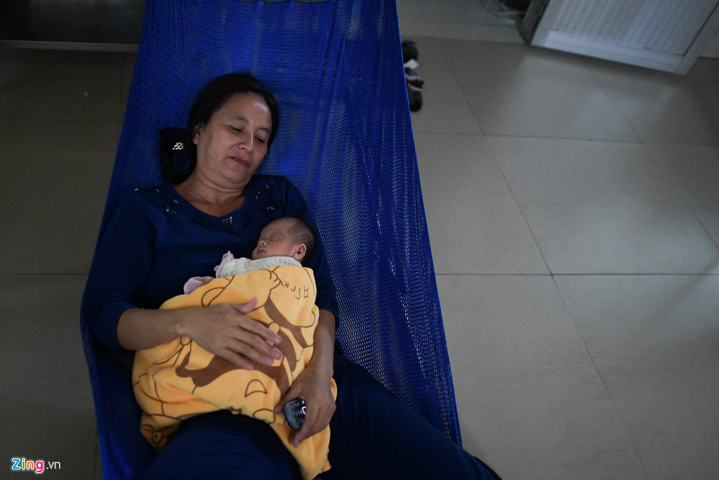 Bà Nguyễn Thị Ngọc Dung (50 tuổi, quê An Giang) tranh thủ nhắm mắt khi cháu ngoại ngủ. Thỉnh thoảng, bà lại xoa lưng cháu ngoại. “Cháu bị viêm phổi gần 2 tháng nay, chưa khỏi hẳn đã xin về, giờ bệnh trở nặng. Ở đây đông quá, muốn về nhà mà bệnh cháu chưa đỡ. Ăn ngủ tạm bợ đôi lúc bất tiện, đau lưng nhưng đành chịu vì bệnh nhân đông, bác sĩ cũng vất vả nhiều”, bà Dung chia sẻ.