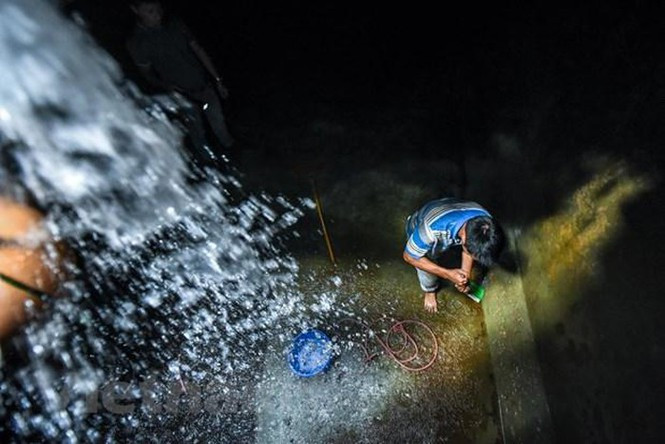 Việc cọ rửa bể tốn khá nhiều thời gian do một số chỗ đọng nước không thể hút bằng máy bơm và phải múc bằng xô sau đó đổ ra ngoài. (Ảnh: PV/Vietnam+)