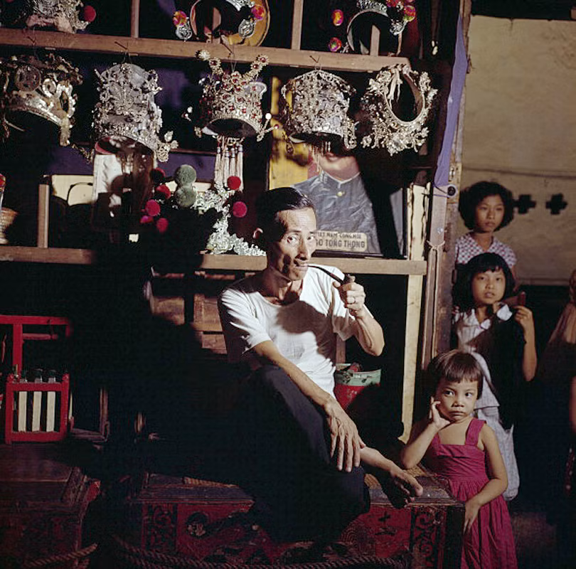 Ông bố người Hoa hút thuốc bằng tẩu bên 3 đứa con gái tại cửa hàng bán trang phục sân khấu của mình ở Chợ Lớn năm 1961.