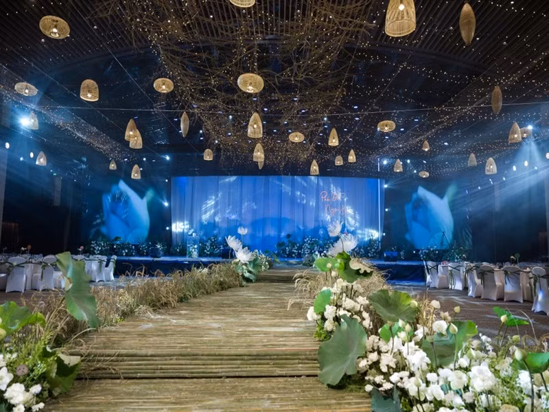 Tối ngày 10/12, đám cưới Hoa hậu Ngọc Hân - Phú Đạt diễn ra tại Hà Nội. Cô dâu mang những đặc trưng văn hóa Bắc bộ vào lễ cưới. Cụ thể, sân khấu chính được thiết kế như một đầm sen vào buổi sáng tinh sương. Những bông hoa sen, lúa nước được sắp xếp tự nhiên. Cây cầu tre nhỏ được làm 100% từ tre tự nhiên, thành lối dẫn đưa cô dâu chú rể bước những bước đi đầu tiên trên con đường hôn nhân. Hội trường được phủ sáng bằng ánh đèn vàng, mô phỏng bầu trời đom đóm. Những chiếc đèn mây tre đan được sử dụng để tạo điểm nhấn. Ảnh: Zing