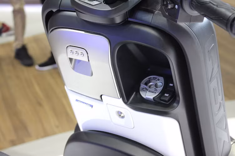 Ở bên dưới, ổ khóa của QBIX là dạng khóa từ y hệt các mẫu xe tay ga tầm trung khác của hãng xe máy Yamaha. Phiên bản cao cấp nhất của xe có khóa thông minh Smartkey. QBIX cũng có ổ điện 12V nằm trong hộc chứa đồ, giúp người sử dụng có thể sạc các thiết bị di động như máy nghe nhạc hay điện thoại nếu có jack chuyển.