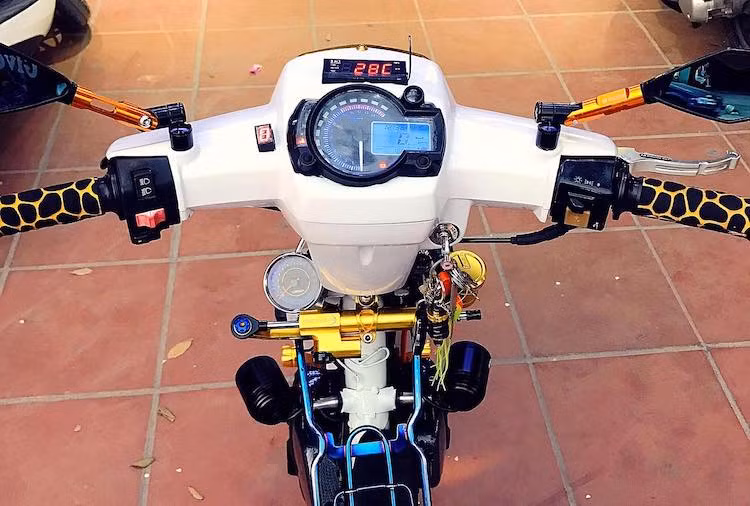 Bên cạnh phần đầu, cụm đồng hồ nguyên bản của Dream cũng đã bị loại bỏ và thay bằng đồng hồ điện tử phong cách Koso RX2N, kèm theo báo số điện tử và đồng hồ Koso Mini 3. Nằm hai bên tay lái là cặp bao tay "vằn vện" sặc sỡ cùng gương chiếu hậu Rizoma đồ chơi, bên dưới là đồng hồ báo tua cùng cây trợ lực Sum Racing cũng có màu vàng bắt mắt.