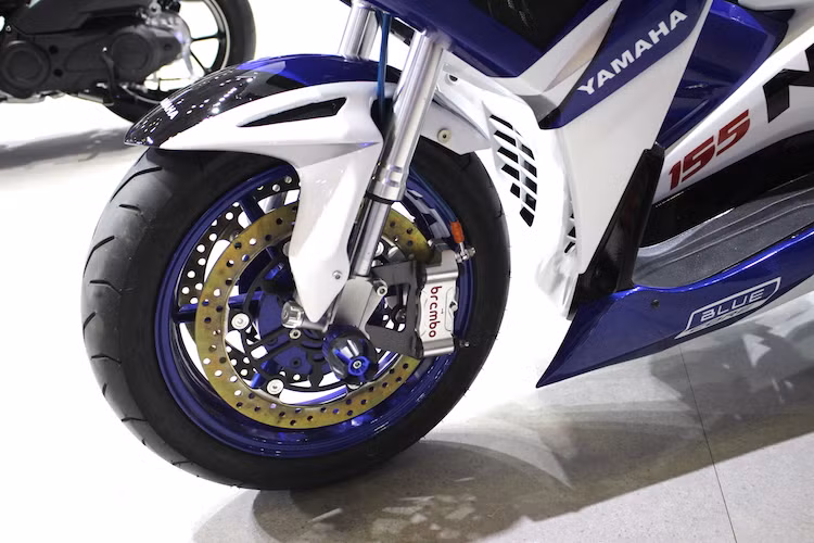 Ở phía trước, toàn bộ "dàn chân" của NVX đã được độ lại. Không chỉ có mâm 6 cây khác biệt so với thiết kế nguyên bản, chiếc xe còn được độ phuộc trước USD khỏe khoắn cùng hệ thống phanh trước nâng cấp đĩa kép logo Yamaha, kèm theo cặp heo Brembo Monoblock 4 pis đồ chơi.