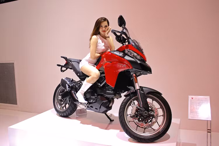 Hãng xe phân khối lớn Ducati có khu trưng bày chia làm 2 phong cách khác nhau, chính vì vậy trang phục của dàn người mẫu cũng đã được "biến hóa" phù hợp. Với các dòng xe ngoài Scrambler, bộ váy trắng của mỗi người đẹp trở nên nổi bật hẳn khi đứng cạnh những chiếc Ducati màu đỏ truyền thống, đen hoặc trắng.