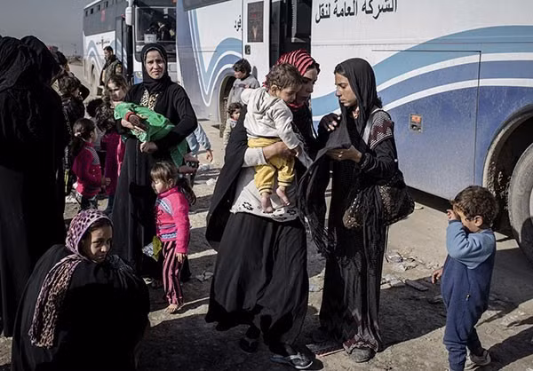 Trẻ em và phụ nữ Iraq đứng chờ xe buýt để đưa họ rời khỏi chảo lửa Mosul. Ảnh FNA