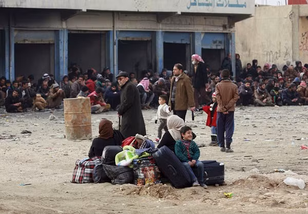 Hàng trăm người ngồi tập trung tại một điểm đón để chờ xe chở tới nơi an toàn hơn. Ảnh FNA