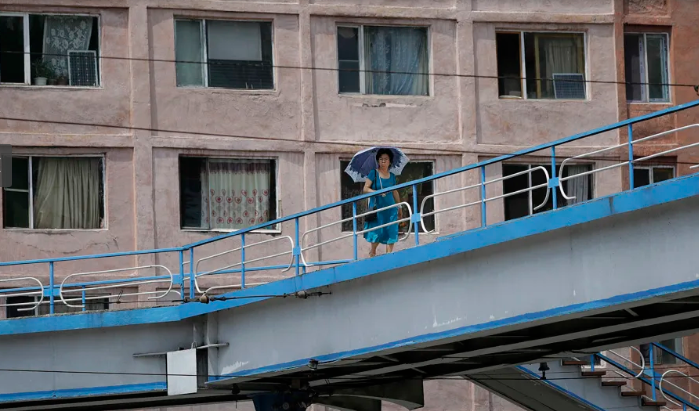 Người phụ nữ che ô đi qua cầu vượt tại Bình Nhưỡng, Triều Tiên. Phía sau cô là một tòa chung cư.