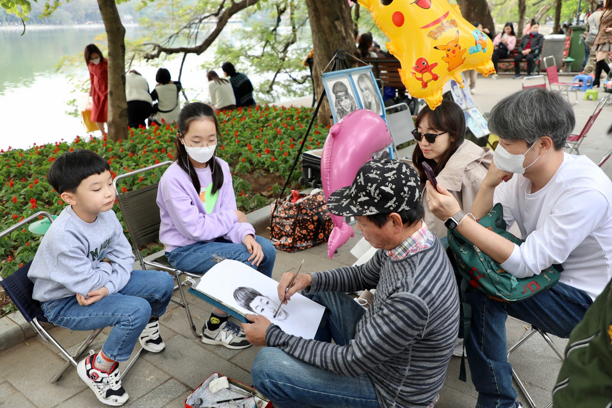 Một gia đình nước ngoài tham gia trải nghiệm vẽ tranh truyền thần tại phố đi bộ Hồ Gươm.