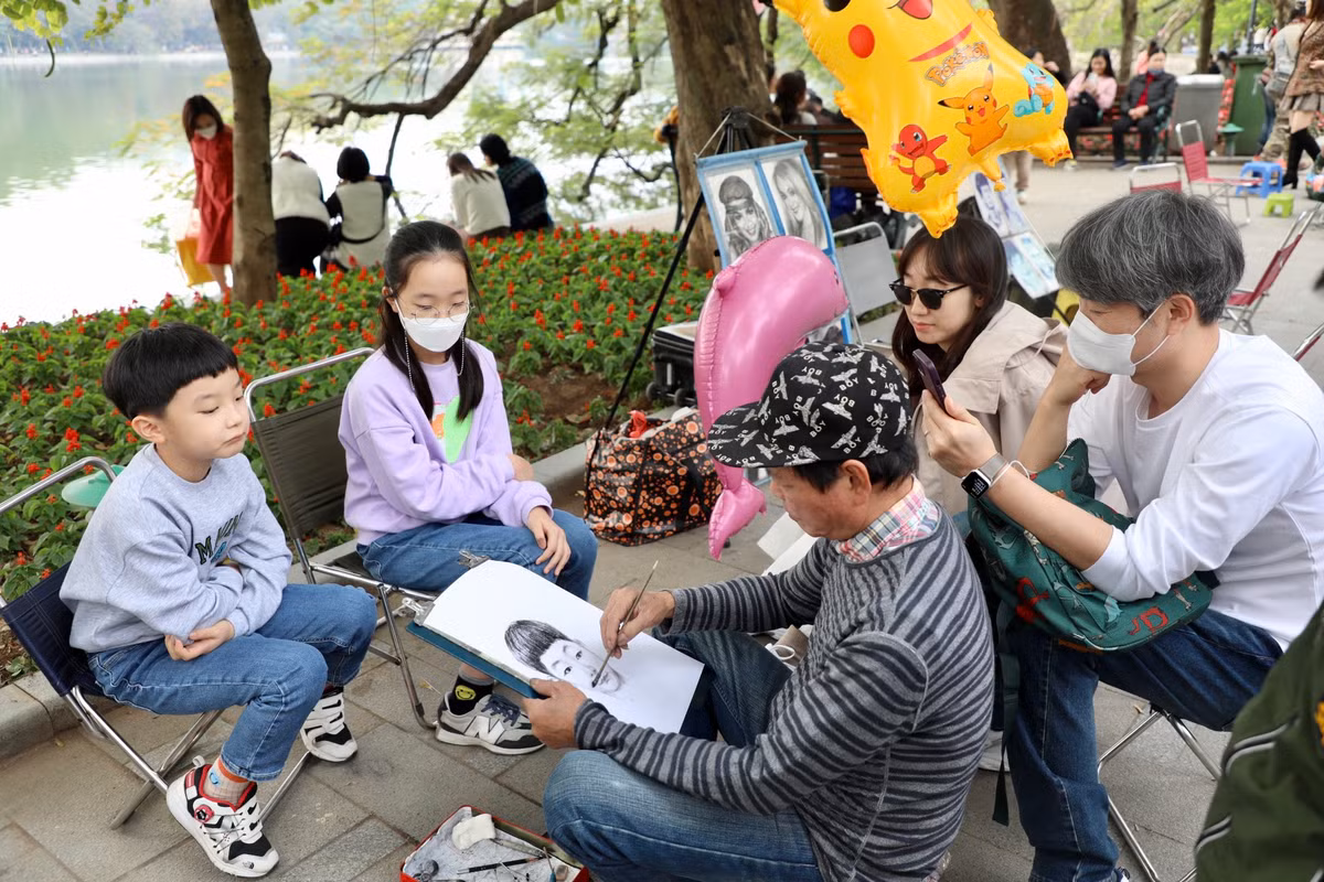 Một gia đình nước ngoài tham gia trải nghiệm vẽ tranh truyền thần tại phố đi bộ Hồ Gươm.