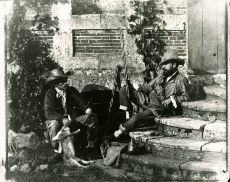 Hai người thợ săn nghỉ ngơi bên bậc cấp của một ngôi nhà, một người cầm trong tay con thỏ mới bắn được, nước Pháp thập niên 1840.