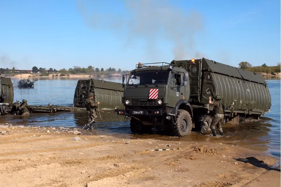 Từng tấm cầu phao được thả xuống nước bằng cách lùi xe nhanh rồi phanh gấp, các tấm cầu phao sẽ theo lực quán tính trôi xuống sông. Nguồn ảnh: Engmil.