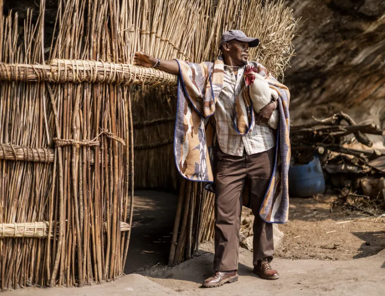 Một số cư dân vẫn sinh sống trong khu hang động này. Ảnh: Ndlovu, 40 tuổi, tạo dáng với một con gà trống trước ngôi nhà.