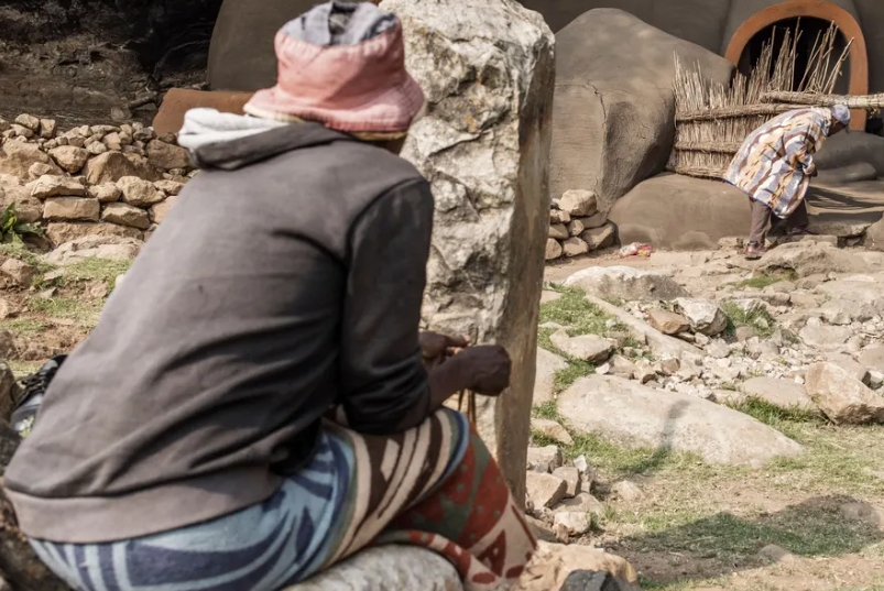 Ndlovu (phải) cúi xuống để đi qua cửa cổng bằng rơm vào nhà.