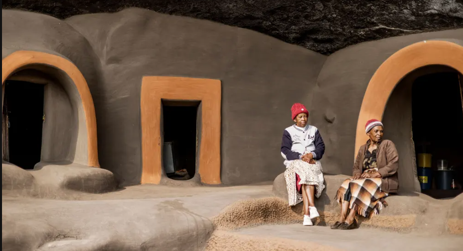 Makoenweo (trái), 60 tuổi, và Mamtsaseng Khutsoane, 66 tuổi, ngồi trước nhà của họ. Cửa ra vào mở vừa đủ cao để từng người có thể đi qua được. Tường và sàn nhà được làm bằng hỗn hợp bùn và phân cần được bảo dưỡng thường xuyên.