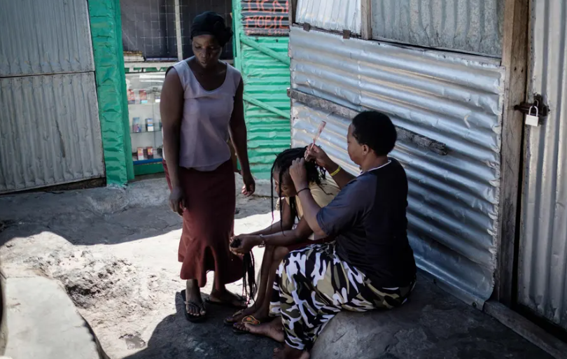 Những người phụ nữ tết tóc cho nhau trong một con hẻm.