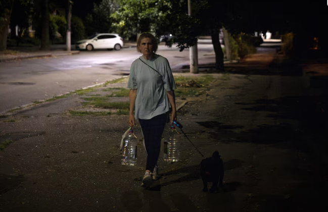 Người phụ nữ mang theo hai chai nước trở về nhà hôm 04/07. Khu vực này cũng đối mặt với tình trạng mất điện.