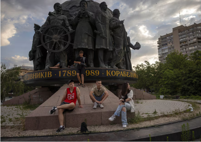 Một số thanh niên ngồi dưới chân tượng đài những người đóng tàu ở thành phố cảng Mykolaiv, Ukraine, ngày 04/07/2024.