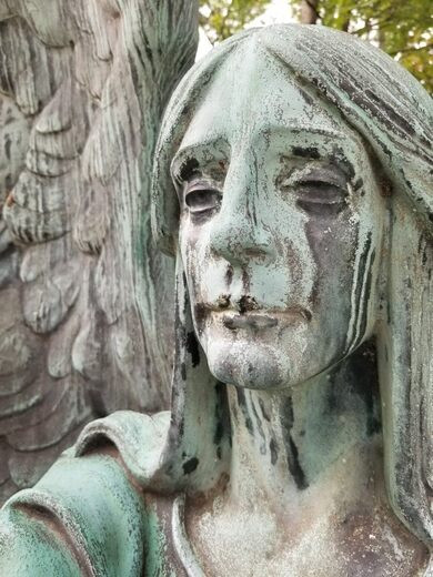 Bức tượng khắc họa hình ảnh thiên thần trong tư thế ngồi với đôi cánh mở rộng và cầm ngược ngọn đuốc.