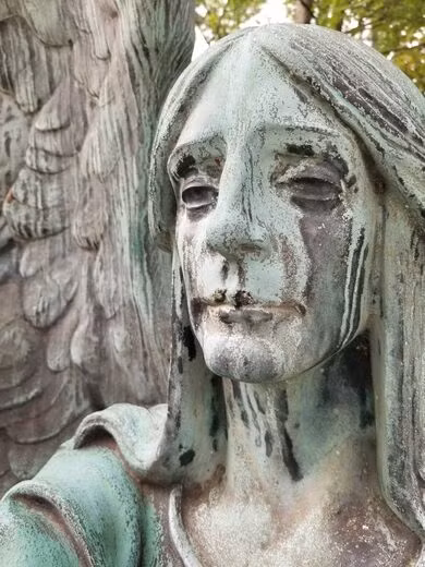 Bức tượng khắc họa hình ảnh thiên thần trong tư thế ngồi với đôi cánh mở rộng và cầm ngược ngọn đuốc.