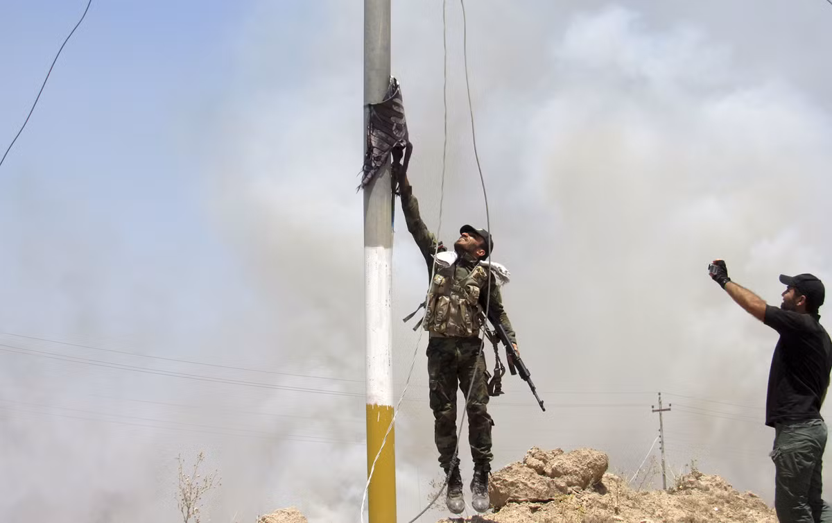 Một chiến binh thuộc Lữ đoàn Badr đang kéo cờ IS xuống.