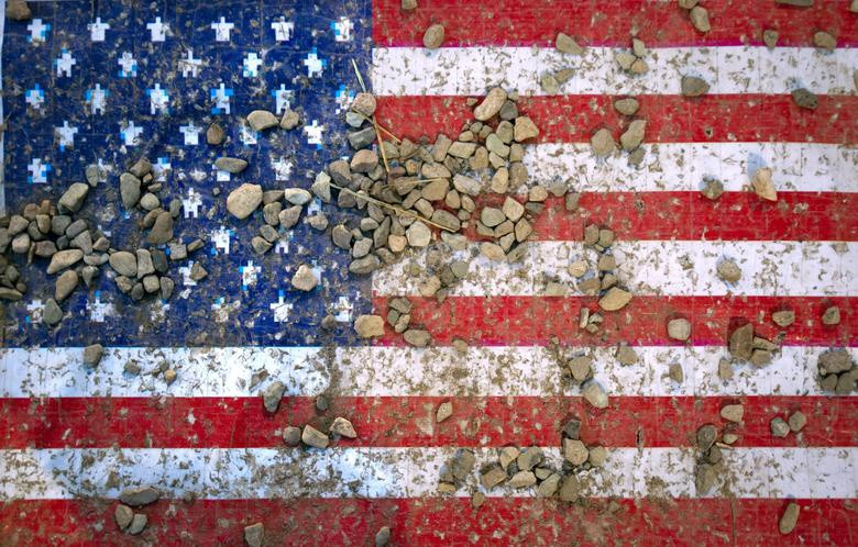 Cờ Mỹ bị rải sỏi đá, trong một triển lãm chiến tranh của Vệ binh Cách mạng để tưởng niệm chiến tranh Iran - Iraq, ở phía nam Tehran, vào tháng 9/2011. Trong nước, Vệ binh Cách mạng Iran coi ảnh hưởng của Mỹ là thách thức lớn, và lập ra các nhóm dân quân tình nguyện (Basij) ở mọi cấp học, mọi văn phòng chính phủ, doanh nghiệp, các thánh đường địa phương nhằm theo dõi, ép buộc người dân ủng hộ lãnh đạo tối cao. Ảnh: Reuters.