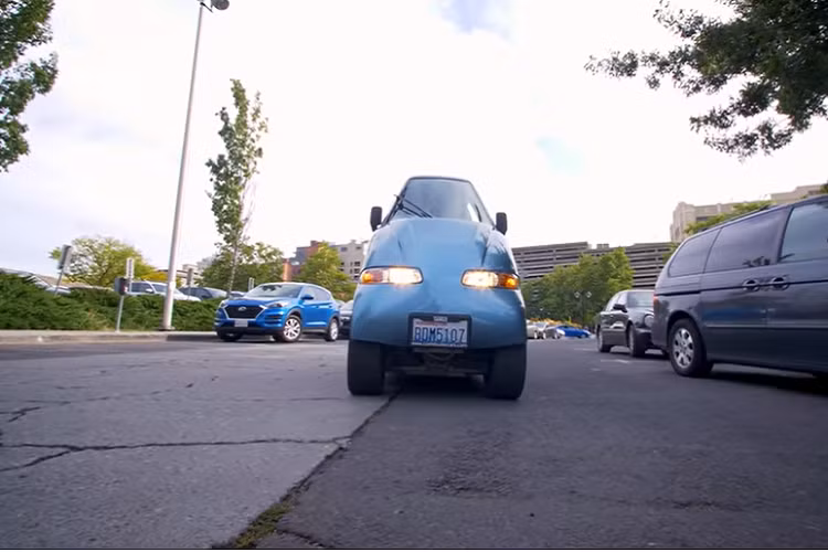 Hồi năm 1998, Rick Woodbury và con trai đã thành lập Commuter Cars ở Spokane, Washington. Phải đi làm hàng ngày bằng xe, Rick nhận ra một điều quan trọng rằng: mọi người đi làm hàng ngày bằng xe cá nhân, mà bên phía hành khách luôn để không. Cân nhắc tình trạng tắc nghẽn giao thông trên thế giới và nhận thấy ý tưởng nhân đôi số làn đường là không thể, Rick nghĩ rằng nếu chế tạo một chiếc xe chỉ chiếm một nửa không gian thì sao? Bằng cách này, người ta có thể nhồi nhét gấp 2 lần số lượng xe lên số làn đường hiện tại.