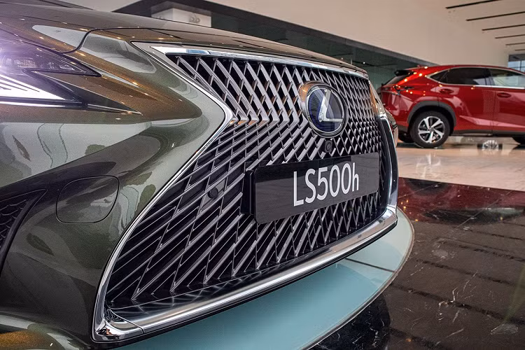 Mẫu sedan hạng sang Lexus LS 500h 2020 sở hữu ngoại thất sang trọng đúng nghĩa với phần đầu xe là lưới tản nhiệt con suốt quen thuộc, các nan được tạo hình đan xen và viền mạ crom. Trung tâm mặt ca-lăng trên Lexus LS500h 2020 bản kỷ niệm là logo thương hiệu 3D kết hợp màu xanh biểu thị đây là xe Hybird kèm camera quan sát phía trước trong gói camera 360 độ mà xe được trang bị.