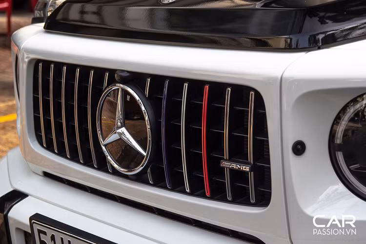 Chiếc Mercedes-AMG G63 này mang màu gốc là màu trắng bóng nhưng đã được phối lại với phong cách hai tông màu quen thuộc trên những mẫu sedan sang trọng. Phần mui xe được dán decal màu đen bóng tương phản, kết hợp với đó chính là decal ba màu đỏ-trắng-xanh mang đậm dấu ấn của chủ sở hữu. Những đường màu này được phối trên các chi tiết như phần cản trước xe, hộp đựng bánh phụ phía sau hay cả họa tiết trên cánh cửa.