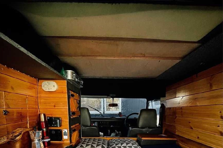 Nhìn bên ngoài, chiếc Land Rover Defender cổ điển này có thân màu xanh đậm với các sọc trắng chạy dọc hai bên. Giá đỡ trên nóc có thể trượt để nhường chỗ cho phần nóc mở lên.