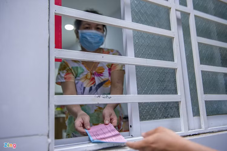 Một người phụ nữ có ý thức hạn chế tiếp xúc với đám đông. Bà mở cửa sổ nhận thẻ vào chợ từ ông Huy.