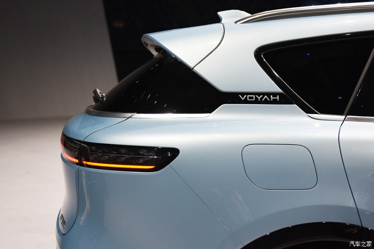Nằm hai bên lưới tản nhiệt là cụm đèn pha hình chữ nhật với 2 bóng LED, vuốt về phía sau. Cụm đèn pha tích hợp dải đèn LED định vị ban ngày, kéo dài đến logo của thương hiệu Voyah ở giữa lưới tản nhiệt. Vòng sang bên sườn, chúng ta sẽ bắt gặp thiết kế khá đơn giản với đường gân nhẹ kéo dài từ chắn bùn trước đến tay nắm cửa thứ hai. Tiếp đến là logo Voyah nằm giữa cột C, tay nắm cửa có thể bật lên/thụt xuống, baga nóc màu bạc và bộ vành đa chấu hình tua-bin khá hút mắt.