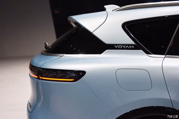 Nằm hai bên lưới tản nhiệt là cụm đèn pha hình chữ nhật với 2 bóng LED, vuốt về phía sau. Cụm đèn pha tích hợp dải đèn LED định vị ban ngày, kéo dài đến logo của thương hiệu Voyah ở giữa lưới tản nhiệt. Vòng sang bên sườn, chúng ta sẽ bắt gặp thiết kế khá đơn giản với đường gân nhẹ kéo dài từ chắn bùn trước đến tay nắm cửa thứ hai. Tiếp đến là logo Voyah nằm giữa cột C, tay nắm cửa có thể bật lên/thụt xuống, baga nóc màu bạc và bộ vành đa chấu hình tua-bin khá hút mắt.