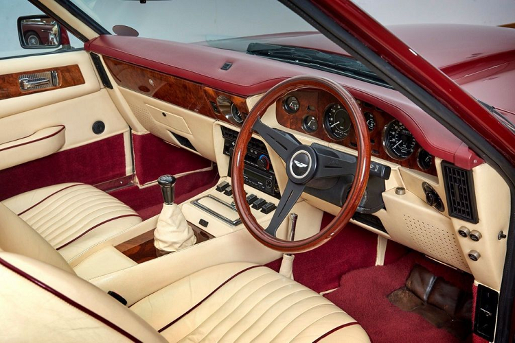Aston Martin V8 Volante 1988 nổi bật với nội thất bọc da màu kem kết hợp cùng các chi tiết làm từ gỗ óc chó trên vô-lăng, khu vực táp-lô...