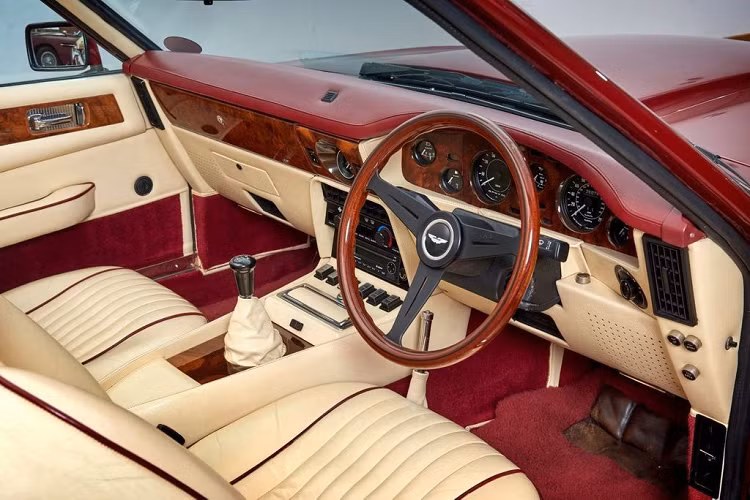 Aston Martin V8 Volante 1988 nổi bật với nội thất bọc da màu kem kết hợp cùng các chi tiết làm từ gỗ óc chó trên vô-lăng, khu vực táp-lô...