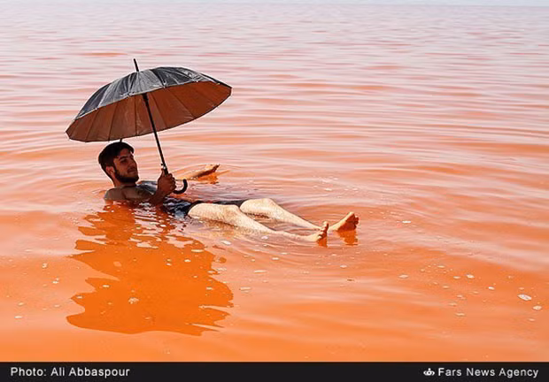 Một người đàn ông đang bơi giữa hồ nước đỏ ở Iran.