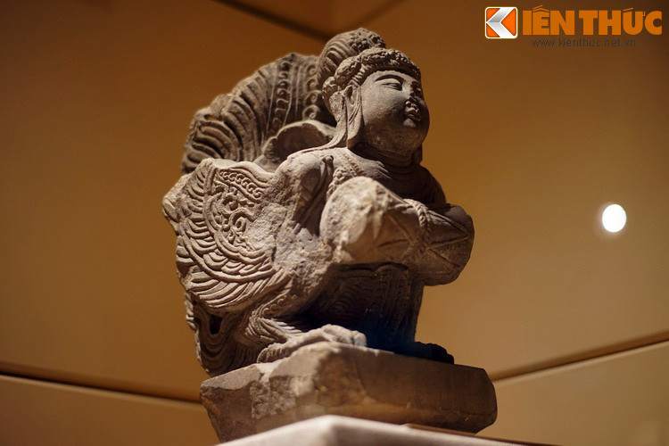 Đôi cánh Kinnara dang rộng, toàn thân ưỡn về phía trước trong tư thế đang bay và hai tay ôm trống tầm bông.