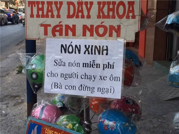 Cửa hàng mũ bảo hiểm kèm "dịch vụ" sửa mũ bảo hiểm miễn phí cho người chạy xe ôm. Người chủ tiệm còn khéo léo nhắc nhở "Bà con đừng ngại" để việc làm của mình tăng thêm phần ý nghĩa.