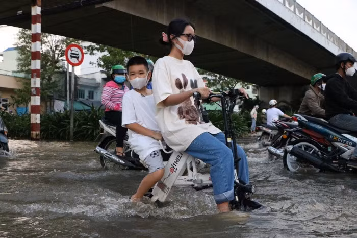 Một cô gái chở theo em trai trên xe điện vượt biển nước về nhà, mặc dù bánh xe lút gần hết.